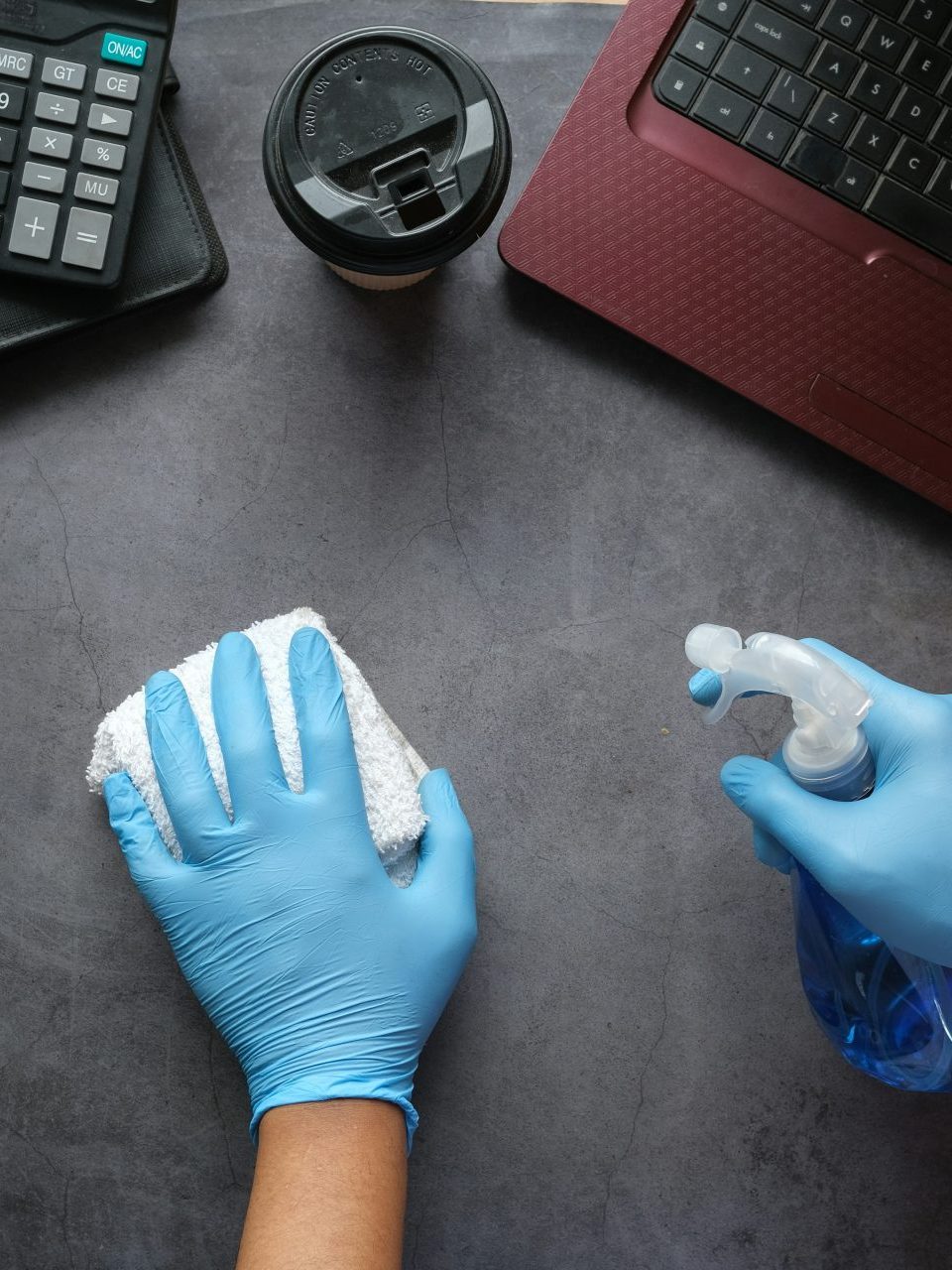 Gloved hands cleaning desk with spray bottle